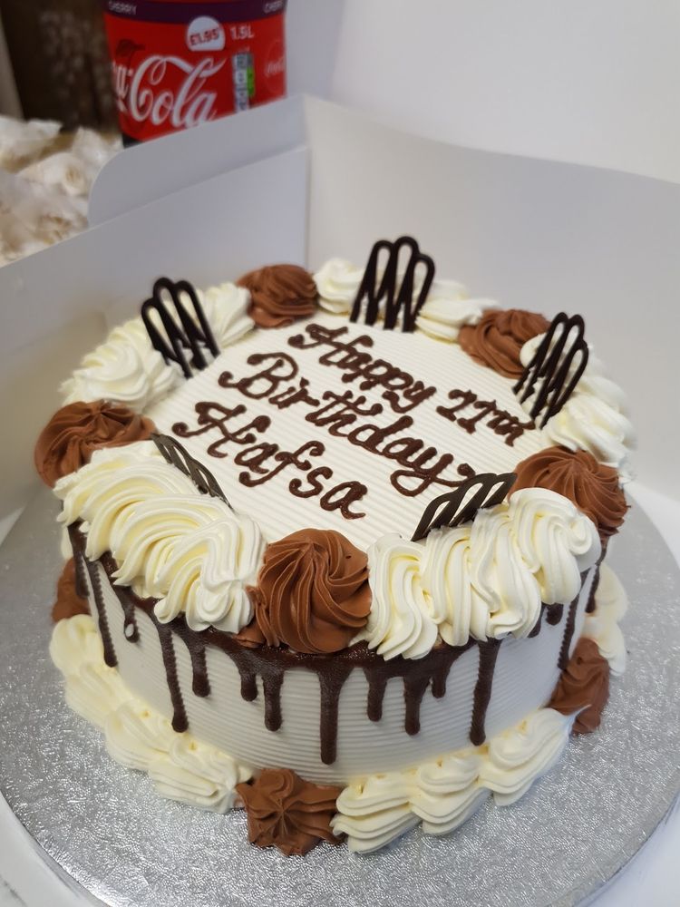 A chocolate-drip celebration cake with piped rosettes, boxed and ready to collect