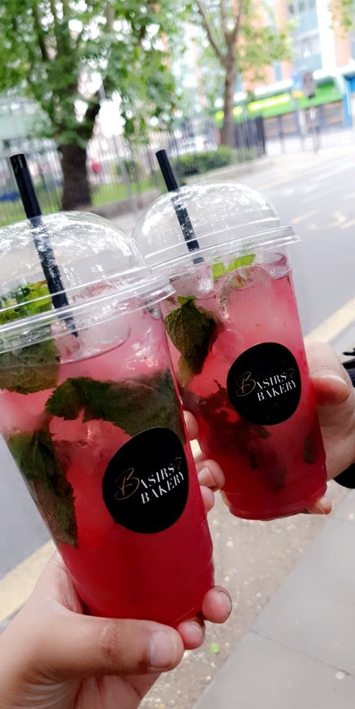 Two hands holding up cups of berry-and-mint mocktail outdoors with trees behind